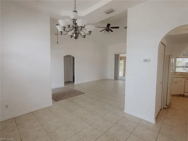 Empty room featuring arched walkways, light tile patterned floors, a towering ceiling, and visible vents