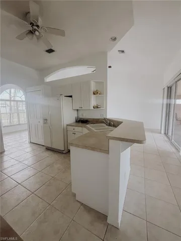Kitchen featuring white refrigerator with ice dispenser, a peninsula, a ceiling fan, light tile patterned flooring, and a sink