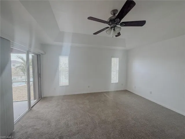 Carpeted empty room with a raised ceiling, baseboards, and a ceiling fan