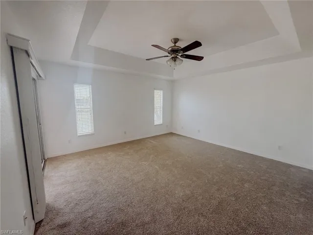 Carpeted empty room featuring plenty of natural light, baseboards, a ceiling fan, and a raised ceiling