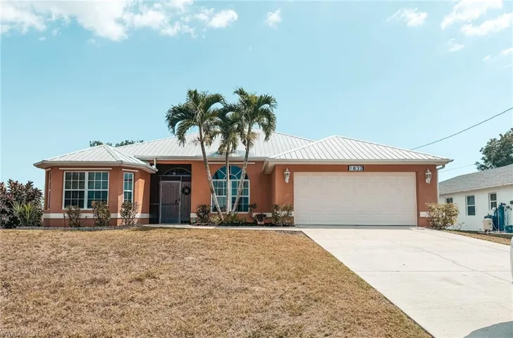 Ranch-style home with stucco siding, driveway, an attached garage, a front lawn, and metal roof