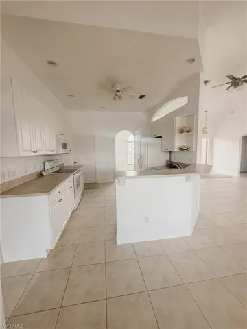 Kitchen featuring a ceiling fan, a peninsula, light tile patterned flooring, and white appliances