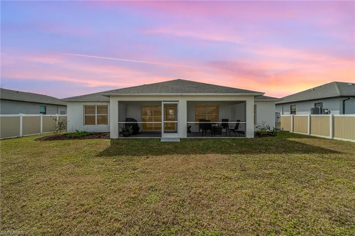 Back house at dusk featuring a lawn and lanai