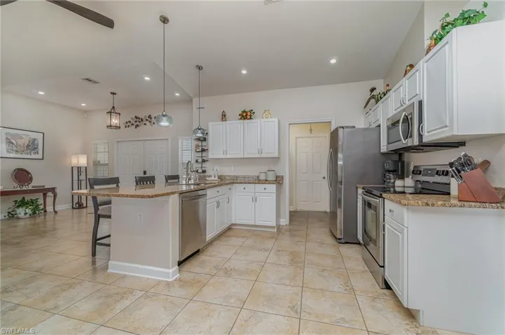 Kitchen with decorative light fixtures, white cabinetry, a breakfast bar area, stainless steel appliances, and light stone counters