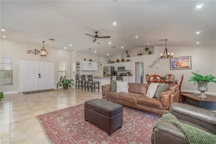 Living room featuring high vaulted ceiling, light tile patterned floors, sink, and ceiling fan with notable chandelier