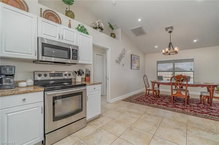Kitchen featuring decorative light fixtures, white cabinets, stainless steel appliances, and lofted ceiling