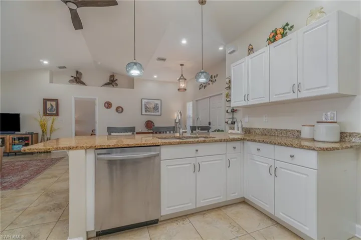 Kitchen featuring kitchen peninsula, pendant lighting, stainless steel dishwasher, white cabinets, and sink
