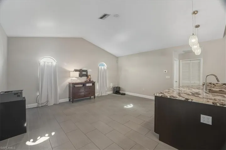 Kitchen with light stone counters, hanging light fixtures, lofted ceiling, and open floor plan