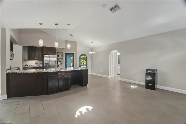 Kitchen featuring arched walkways, dark wood finish cabinetry, a peninsula, light stone counters, and stainless steel appliances