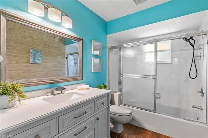 Full bathroom with vanity, toilet, wood-type flooring, and bath / shower combo with glass door