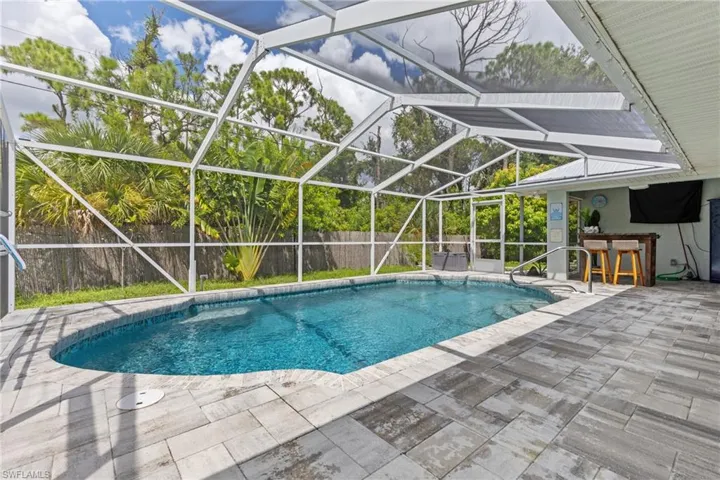 View of swimming pool with an outdoor bar, glass enclosure, and a patio area
