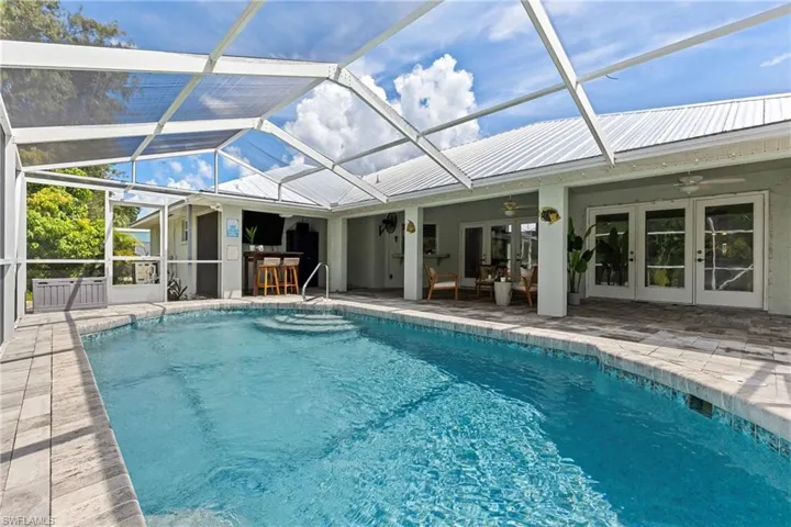 View of swimming pool with glass enclosure, ceiling fan, a patio area, and french doors
