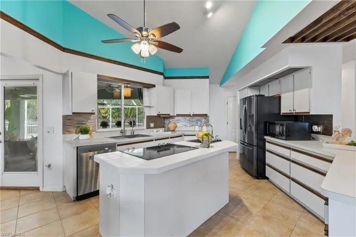 Kitchen with black appliances, tasteful backsplash, a center island with sink, and ceiling fan