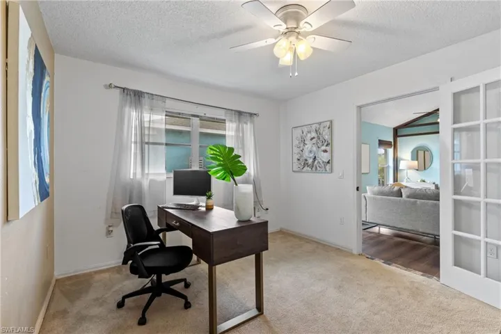 Office space with vaulted ceiling, light colored carpet, ceiling fan, and a textured ceiling