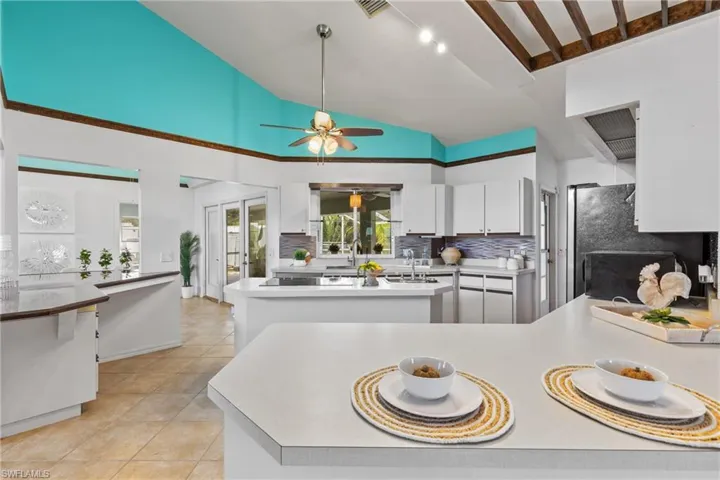Kitchen featuring fridge, light tile patterned floors, ceiling fan, decorative backsplash, and vaulted ceiling