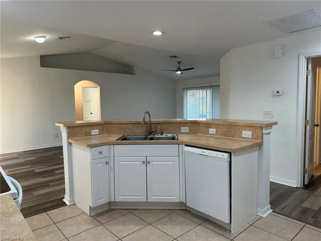 Kitchen with an island with sink, white cabinetry, arched walkways, white appliances, and ceiling fan