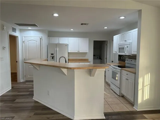 Kitchen with white cabinets, white appliances, light countertops, a kitchen breakfast bar, and recessed lighting