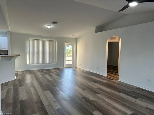 Unfurnished living room featuring dark wood-style floors, arched walkways, ceiling fan, and lofted ceiling