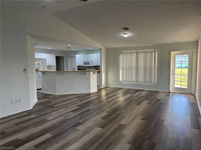 Unfurnished living room with lofted ceiling, dark wood-style flooring, and recessed lighting