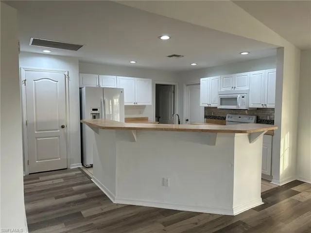 Kitchen featuring white appliances, white cabinets, light countertops, an island with sink, and recessed lighting