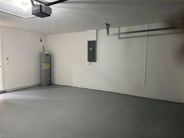 Garage with water heater, electric panel, and a garage door opener