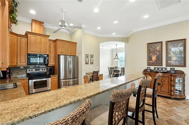 Kitchen featuring ornamental molding, arched walkways, stainless steel appliances, light stone counters, and decorative backsplash