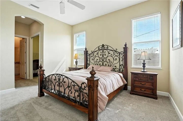 Bedroom featuring light colored carpet, arched walkways, a ceiling fan, and ensuite bath