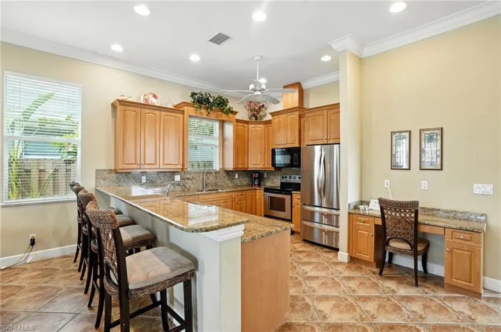 Kitchen with backsplash, light stone counters, appliances with stainless steel finishes, a breakfast bar, and ornamental molding