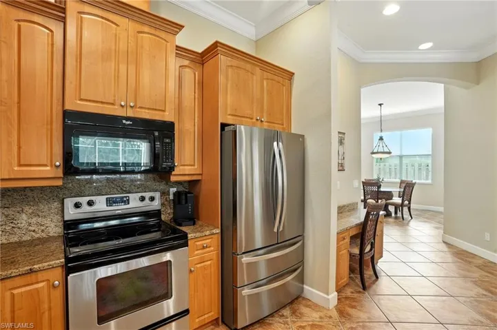 Kitchen with appliances with stainless steel finishes, ornamental molding, light tile patterned flooring, backsplash, and dark stone countertops