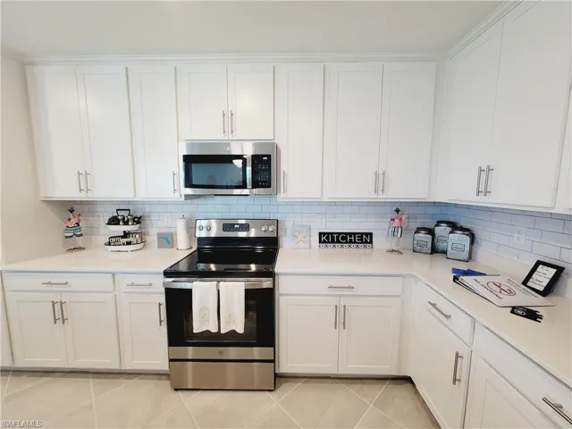Kitchen with tasteful backsplash, white cabinetry, appliances with stainless steel finishes, and light tile patterned floors