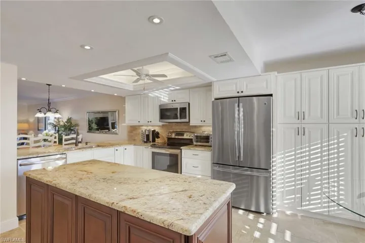 Kitchen with a tray ceiling, ornamental molding, light stone counters, stainless steel appliances, and decorative backsplash