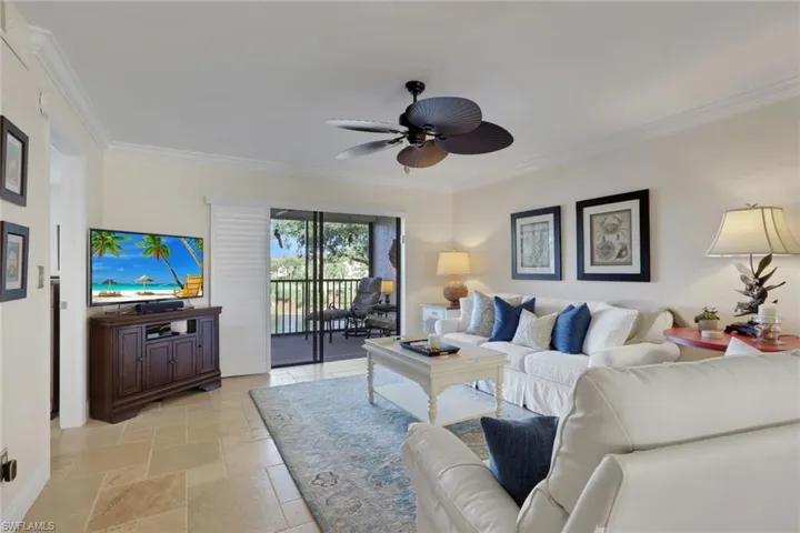 Living room featuring stone tile floors, ornamental molding, and ceiling fan