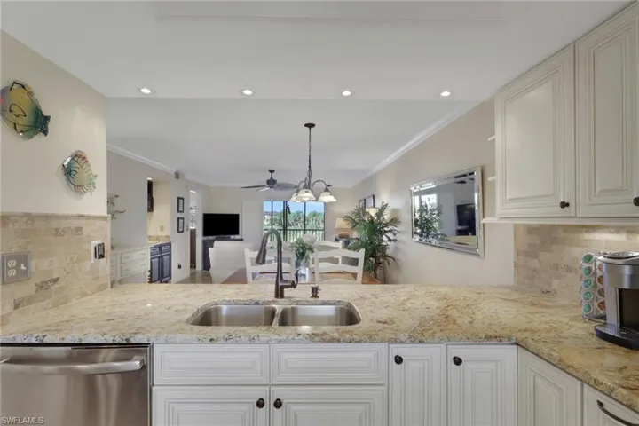 Kitchen featuring backsplash, light stone countertops, stainless steel dishwasher, and crown molding