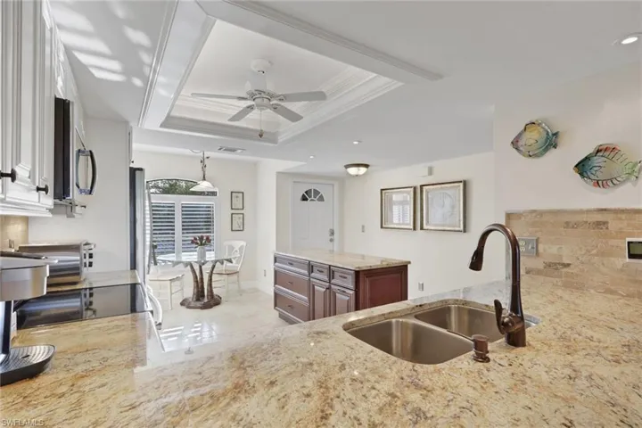 Kitchen featuring light stone counters, a ceiling fan, stainless steel appliances, a raised ceiling, and ornamental molding