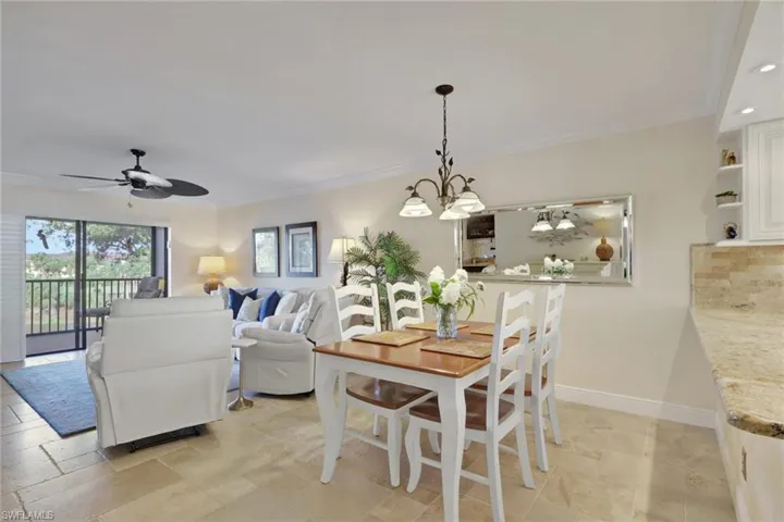 Dining space with ceiling fan, ornamental molding, suspended lighting, and stone tile flooring