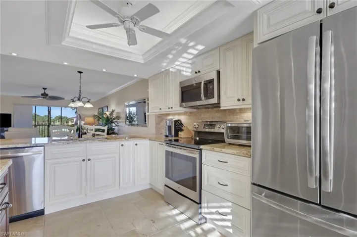 Kitchen with crown molding, stainless steel appliances, a ceiling fan, light stone countertops, and hanging lights