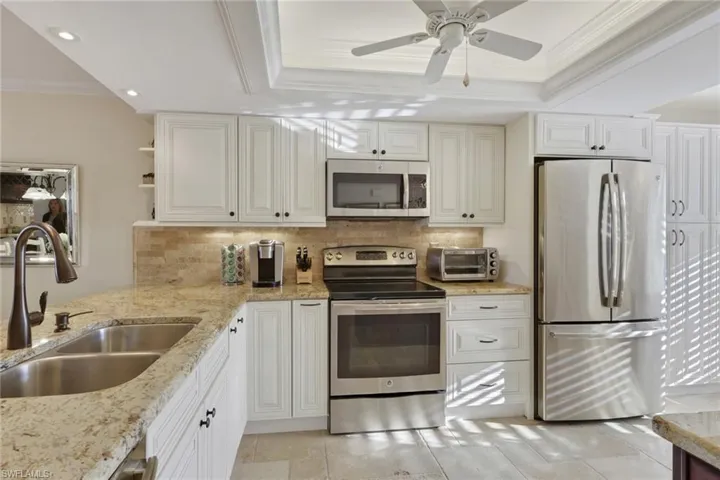 Kitchen featuring crown molding, stainless steel appliances, decorative backsplash, light stone countertops, and open shelves