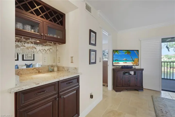 Bar featuring dark wood finish cabinets, glass fronted cabinets, light stone counters, ornamental molding, and stone tile floors