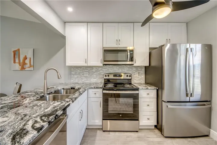 Kitchen featuring backsplash, light stone counters, white cabinets, and stainless steel appliances