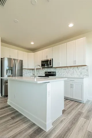 Kitchen featuring white cabinets, light wood-type flooring, stainless steel appliances, and a kitchen island with sink
