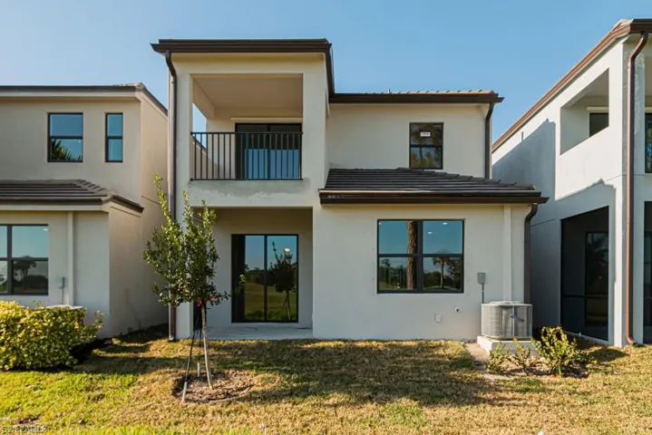Back of house featuring a yard, a balcony, and central AC unit