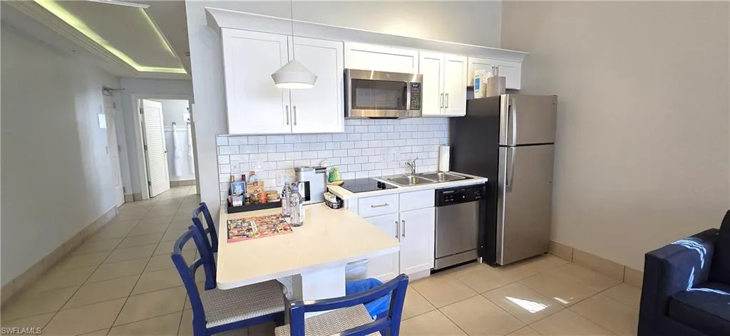 Kitchen featuring white cabinets, light countertops, appliances with stainless steel finishes, pendant lighting, and light tile patterned floors