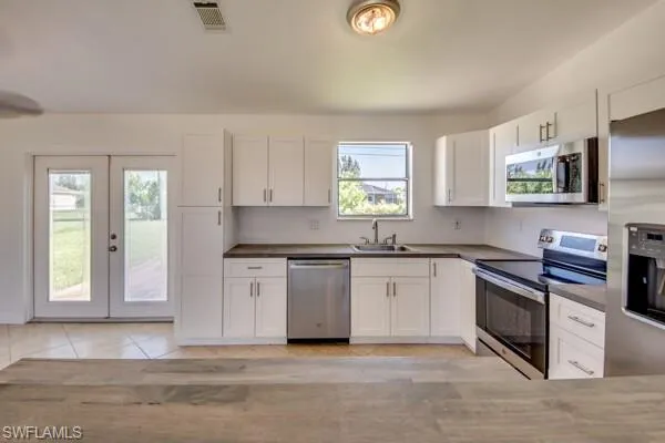 Kitchen with stainless steel appliances, white cabinets, light tile patterned floors, dark countertops, and french doors