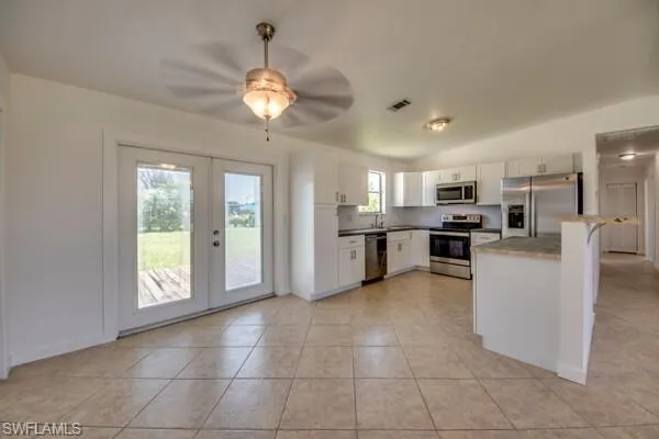 Kitchen featuring stainless steel appliances, a ceiling fan, french doors, white cabinetry, and vaulted ceiling