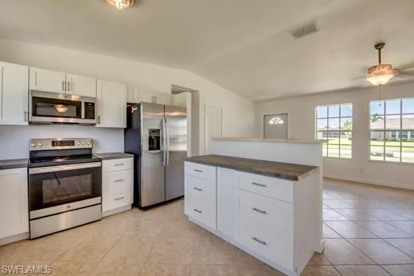 Kitchen with stainless steel appliances, a center island, white cabinets, a ceiling fan, and vaulted ceiling