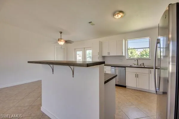 Kitchen featuring stainless steel appliances, a kitchen breakfast bar, dark countertops, and white cabinets