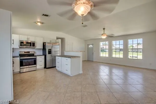 Kitchen with stainless steel appliances, white cabinets, dark countertops, vaulted ceiling, and open floor plan