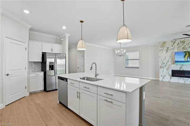 Kitchen featuring decorative light fixtures, white cabinetry, wood finish floors, stainless steel appliances, and ornamental molding