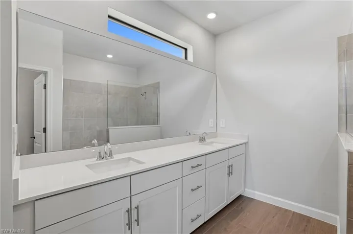 Bathroom featuring wood finish floors, double vanity, a walk in shower, and recessed lighting