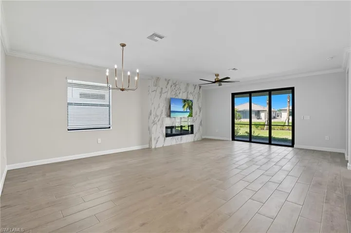 Unfurnished living room featuring a ceiling fan, light wood-type flooring, a fireplace, crown molding, and a chandelier